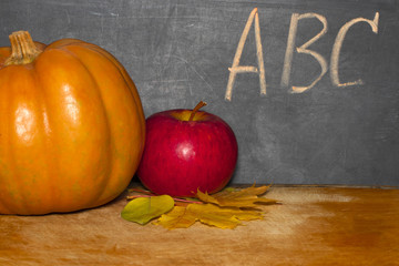 Apple and pumpkin on classroom table in front of blackboard