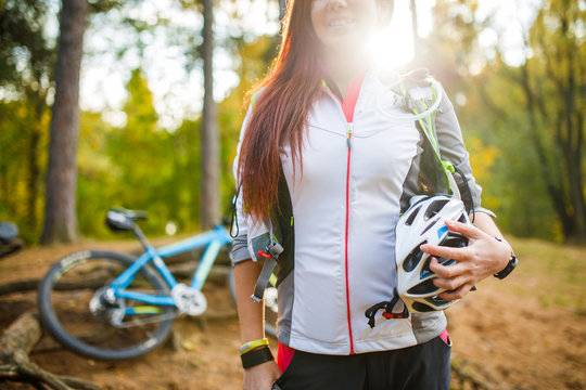 Photo of young sporty woman with helmet on background of bicycle at autumn forest