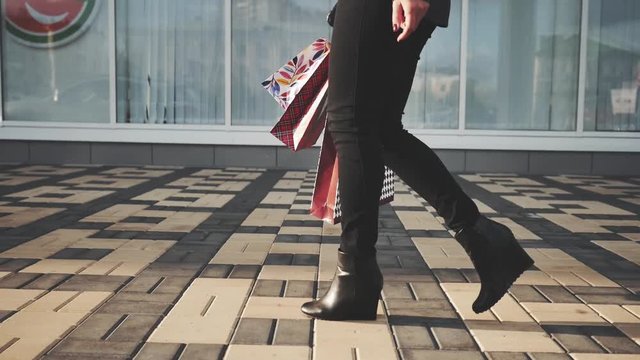 Sexy woman legs in black platform shoes and black jeans with Shopping Bags walking in the city urban street. Steadicam stabilized shot in Slow motion.