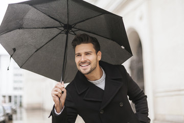 Handsome man with umbrella smiling in the rain