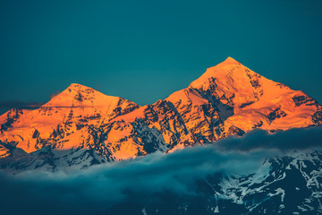 Plakaty  Evening view of sunset over the snowy mountain peak with misty clouds. Travel and nature background. Holiday, travel, sport, recreation. Kazbegi National Park, Gergeti, Georgia. Retro toning filter