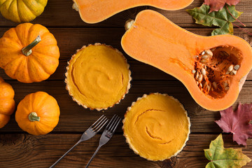 Autumn dessert. Small simple pumpkin pies with decorative pumpkins and butternut squash on rustic wooden background