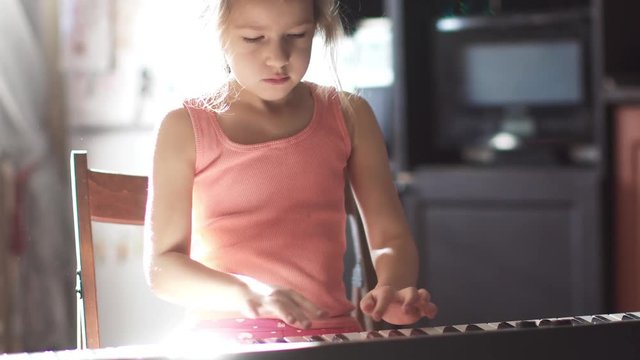 child is playing the piano at home. the little girl is learning to play the electronic piano. girl in the sunlight
