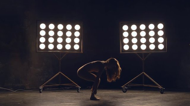 a young woman of pleasant appearance dances in the training hall in the lighting of searchlights in the background. the girl professional dance performs the set number in the style of classical and