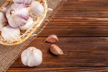 Garlic horizontal banner. Eco farming concept. Whole garlics and cloves in straw basket on piece of sacking on brown wooden texture background. Organic food.