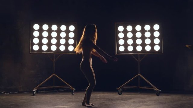a young woman of pleasant appearance dances in the training hall in the lighting of searchlights in the background. the girl professional dance performs the set number in the style of classical and