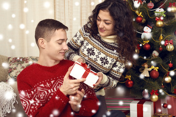 Happy couple give gifts in christmas decoration at home. New year eve, ornated fir tree. Winter holiday and love concept.