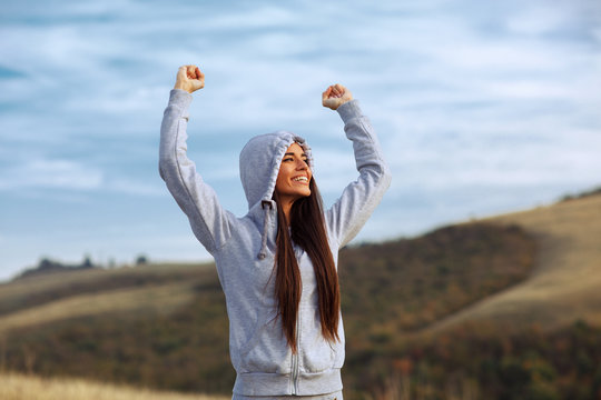 Young sport woman with raised arms motivates herself in nature