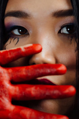 close-up portrait of a young, beautiful Asian girl on Halloween. woman covering her face bloody hand.