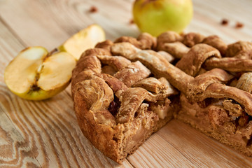 Sliced homemade american apple pie with fresh apples on brown wooden table. Homemade classical fruit tart with raisins. Close up view