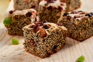 Pieces of poppies cake with raisins and candied fruits on bron wooden background. Close up view
