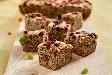 Pieces of poppies cake with raisins and candied fruits on bron wooden background. Side view