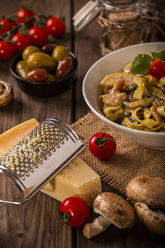 chicken and mushroom tagliatelle shot on wood boards at an angle close-up with a copper pot loose mushrooms vine tomato parmesan block grater basil portrait