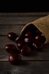  Chestnuts strewing from a bag on a wooden background in dark tones with a leaf with a very high color