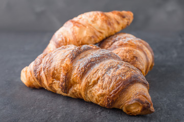 Three croissant sprinkled with powdered sugar on a gray background