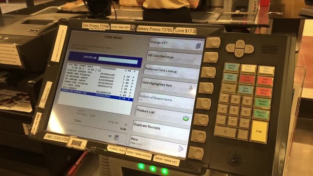 Checkout counter at grocery store point of sale station with computer screen and fingers keying in numbers at end.  