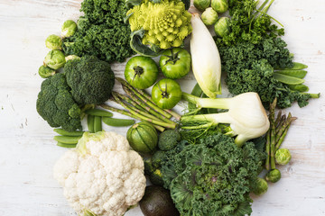 Assortment of green vegetables forming a circle on the white wooden table, copy space for text, top view, selective focus