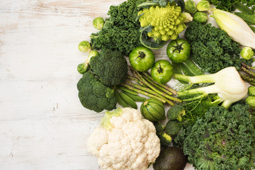 Assortment of green vegetables forming a circle on the white wooden table, copy space for text, top view, selective focus