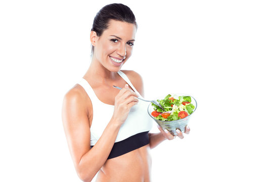 Beautiful young woman eating salad over white background.