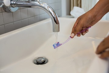 Cropped hands of woman cleaning brush in sink