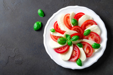 Sliced tomatoes and mozzarella on a white plate, dark stone background. Top view, copyspace