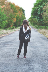 Vertical and Rear view of sad woman with scarf on the head near the empty forest road. Concept of waiting and sadness