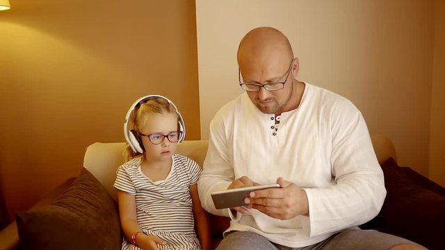 The father shows his daughter how to use the tablet and turned on the music for the girl, the baby put on headphones