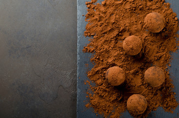 Homemade truffle candies with cocoa powder on a slate plate, dark stone background. Top view,...