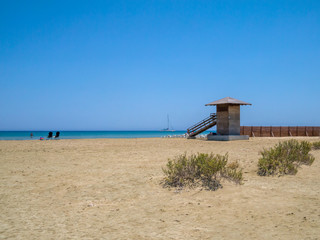 Cyprus beach in early summer with a blue sky, blue sea and sail boat on the horizon.
