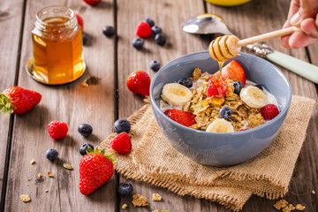 breakfast cereal shot on linen cloth wood boards angled view with raspberries blueberries sliced bananas strawberries with hand swirling honey landscape