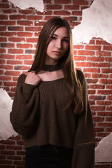 Naklejka premium Model test of fabulous brunette model with long hair, wears oversize sweater, posing on a brick wall background