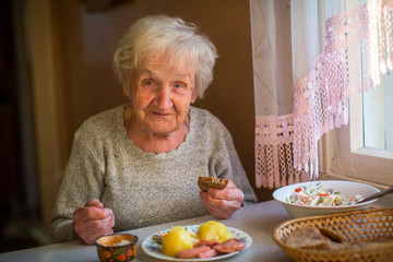 An elderly woman eats at home.