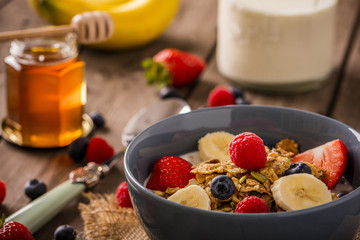 breakfast cereal close-up shot on wood boards angled view with raspberry blueberry banana strawberry and a milk bottle and spoon landscape
