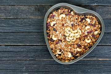 Granola with cashew in a heart-shaped baking dish. Black wooden table
