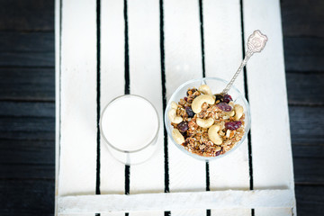 Glass of yogurt and a bowl with granola on a white wooden box