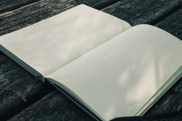Blank empty moleskine notepad in three quarters view from top on wooden table in a park