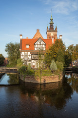 Miller's House (Dom Mlynarza) at Mill Island on Raduni Canal in Gdansk's Old Town in Poland on a sunny day. It's the old headquarters of the Millers guild. St. Cathrine's Church is in the background.