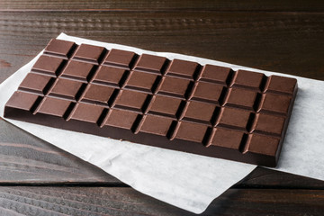 Bitter, dark chocolate bar on wooden planks background