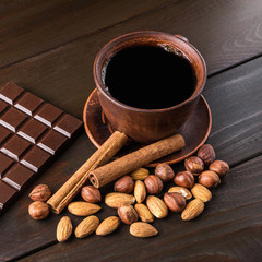 Hot black coffee in brown clay cup, dark chocolate bar, almond, hazelnut and cinnamon stick on...