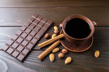Hot black coffee in brown clay cup, dark chocolate bar, almond, hazelnut and cinnamon stick on...