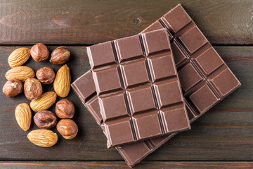 Bitter, dark chocolate bar, almond and hazelnut on wooden background, top view