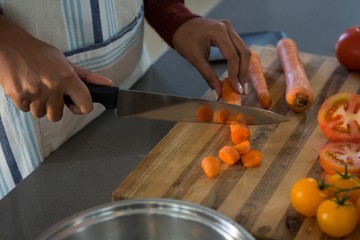 Mid section of woman cutting carrot in kitchen