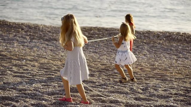 Little girls are playing with a rope on the beach on a warm summer day, the children are near the sea