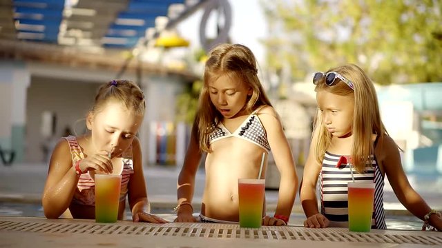 Several sisters are in a swimming pool, children drink soft drinks and talk to each other on a summer day