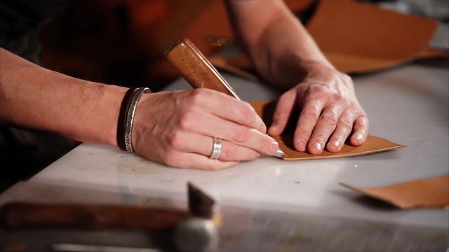 close up shot of the master of the hand, who works with leather products, the person holds a sharp knife on patterns to create marks on the product