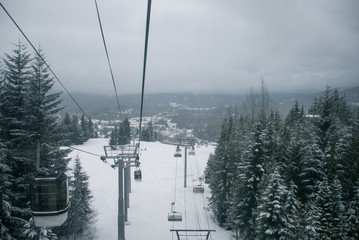 Ski chairlift and gondola going up snow covered mountain between trees © Simon