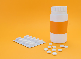 Pills spilling from an open bottle isolated on orange  background