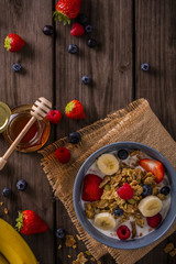 breakfast cereal shot on wood boards top view with raspberries blueberries banana strawberries honey and a  spoon portrait