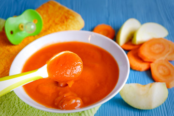puree of baby carrot Apple on a wooden table spoon saucer white green pacifier napkin orange