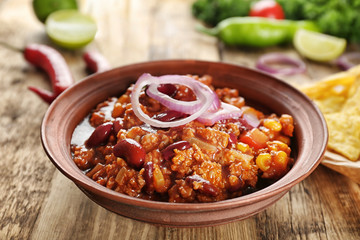 Chili con carne served in bowl with onion rings on kitchen table